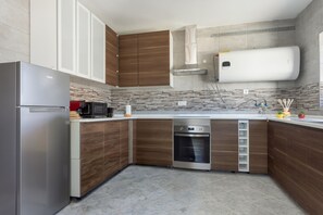 Una cocina moderna con armarios de madera, un refrigerador de acero inoxidable, un horno empotrado y un calentador de agua blanco.