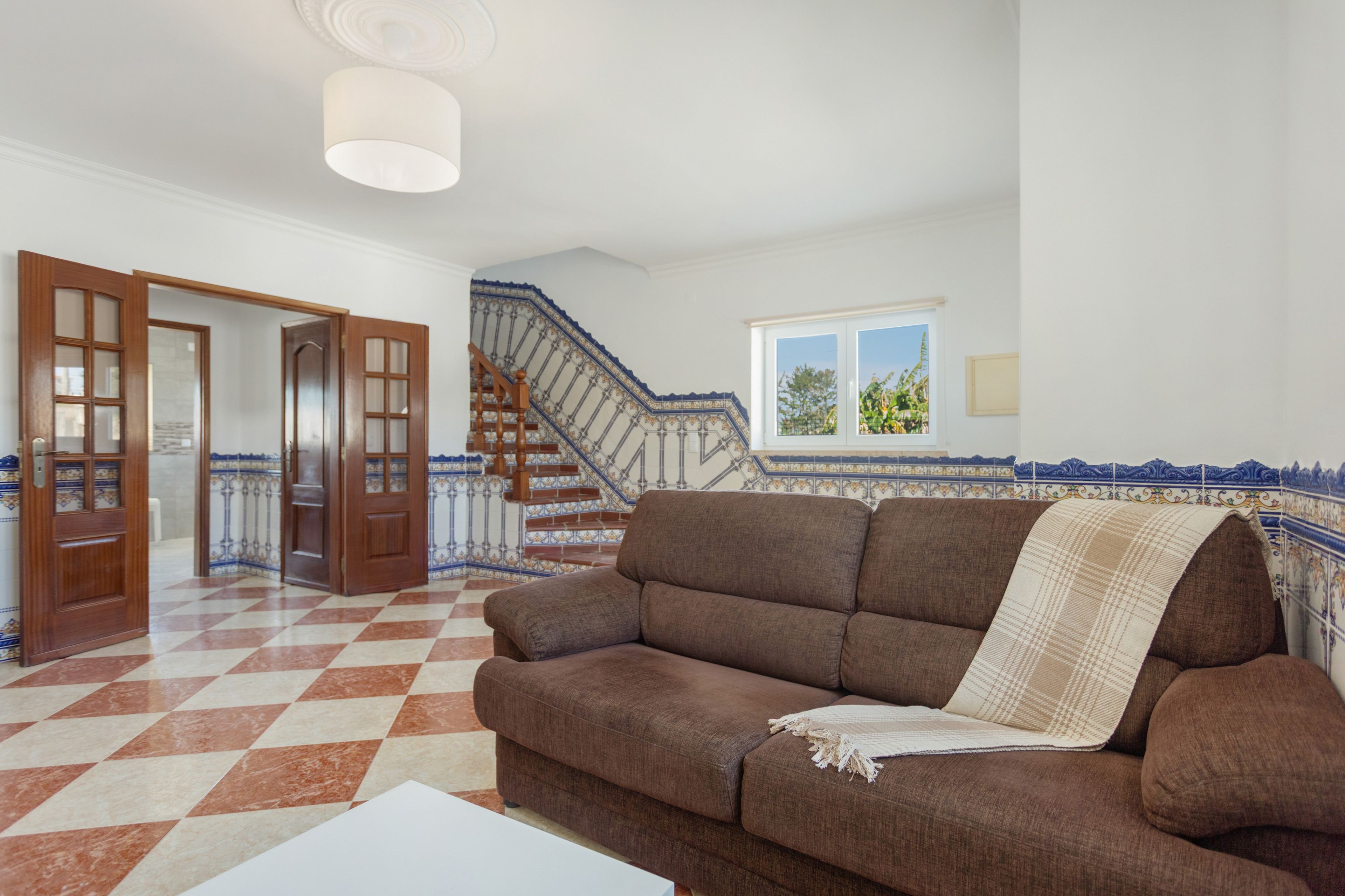 Ein Wohnzimmer mit Schachbrettfußboden, einem braunen Sofa und einer Treppe mit blau-weißen Fliesen.