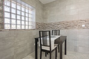 A dining area with a table and chairs, a window with a grid pattern, and a stone accent wall. - Villa 'Bekas House' with private garden, balcony and Wi-Fi (Usseira)