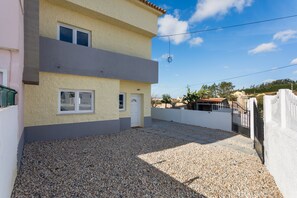 A two-story building with a flat roof, a gravel driveway, and a white door. - Villa 'Bekas House' with private garden, balcony and Wi-Fi (Usseira)