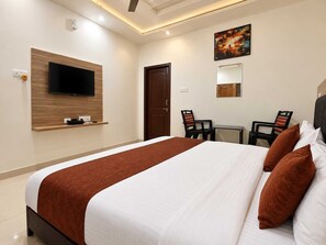 A hotel room with a bed, a television mounted on the wall, a desk with two chairs, and a door. - Classic Advik Cottage (Bhubaneshwar)
