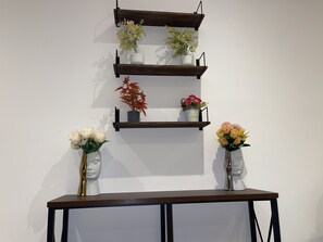 A wall-mounted shelf with three tiers, each holding different types of flowers and decorative items. - Luxurious 1-bedroom apartment Airport Residential (Accra)