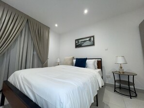 A hotel room with a bed, two bedside lamps, a nightstand, a framed picture on the wall, and a window with curtains. - Luxurious 1-bedroom apartment Airport Residential (Accra)