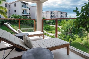 Ein Balkon mit Liegestuhl und kleinem Tisch, mit Blick auf ein Wohngebiet mit Gebäuden und Grünflächen.