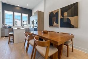 A modern kitchen with a dining area, wooden furniture, and abstract wall art. - Downtown Round Rock, Steps to Main St (Round Rock)