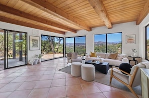 A spacious living area with a wooden ceiling, large windows offering a view of the landscape, and a modern interior design. - Hillview Ranch Retreat A/C Views 16+ guests (Fallbrook)