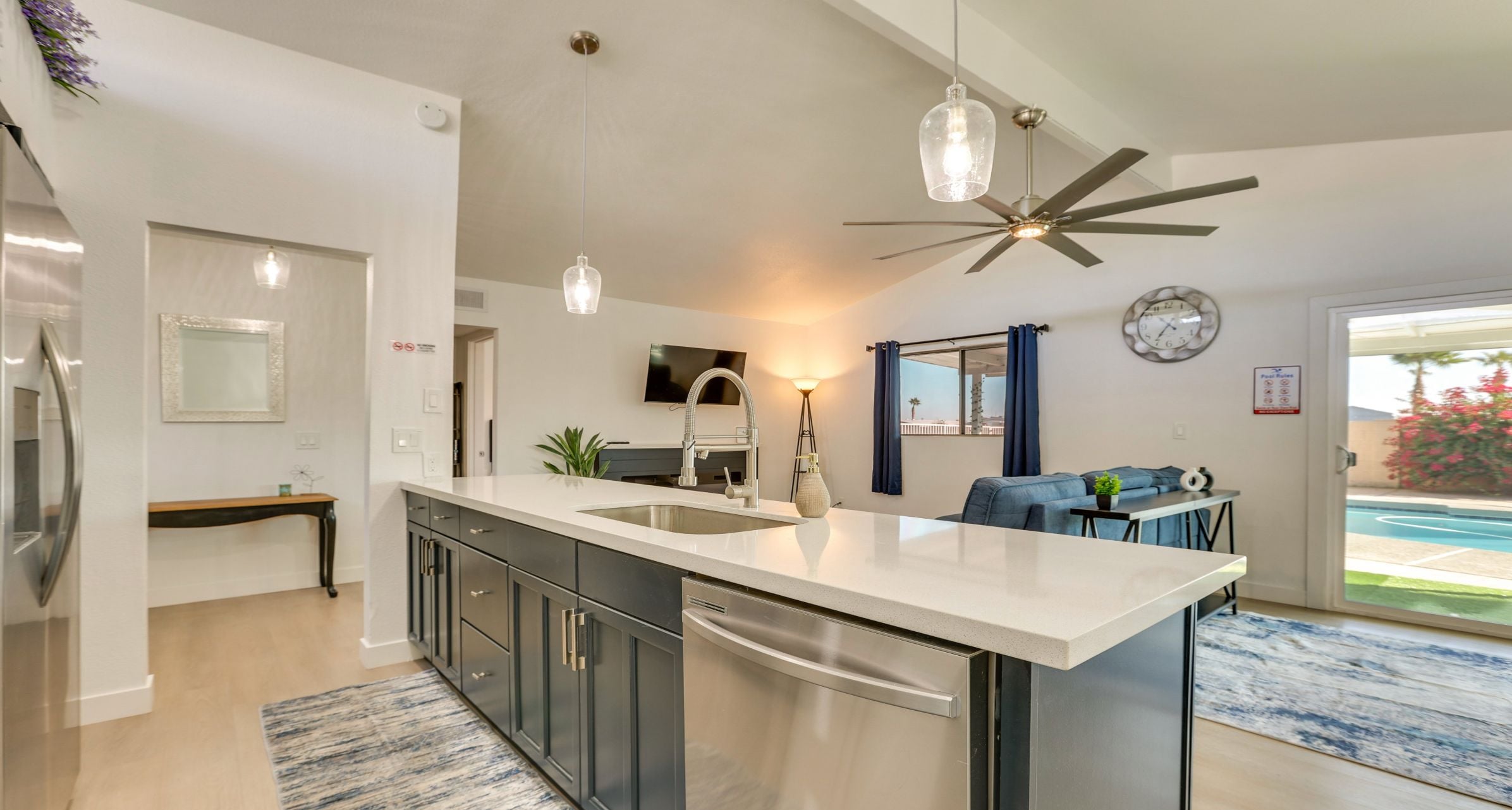 Une cuisine moderne dotée d’un îlot central, d’appareils électroménagers en acier inoxydable, de luminaires suspendus et d’un ventilateur de plafond.