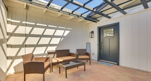 A covered patio with wicker furniture and a glass table, a dark door, and a welcome mat. - Private Pool Oasis | Near Tempe Diablo Stadium (Phoenix)