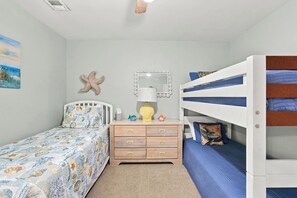 A bedroom with a bunk bed, a single bed with a starfish decoration, a dresser, a mirror, and a painting of a beach scene. - A Little Piece of Heaven | 4BR w/ Oceanfront Decks, Direct Beach Access & Views (Ocean Isle Beach)