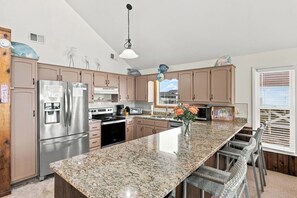 A kitchen with granite countertops, stainless steel appliances, and a large island with bar stools. - A Little Piece of Heaven | 4BR w/ Oceanfront Decks, Direct Beach Access & Views (Ocean Isle Beach)