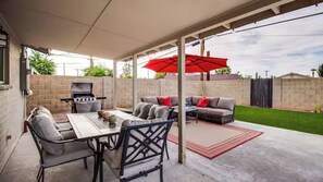 Eine überdachte Terrasse mit Grill, Gartenmöbeln und einem roten Sonnenschirm.