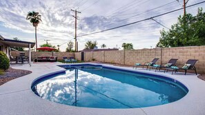 Ein Pool mit geschwungener Kante, umgeben von Liegestühlen und einer überdachten Terrasse.