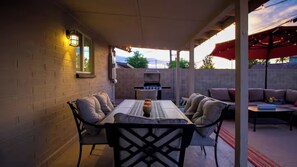 Um pátio externo com mesa e cadeiras, churrasqueira e área de estar coberta.