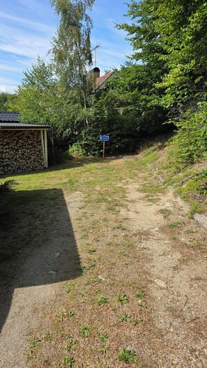 Ein Kiesweg führt zu einem Gebäude mit einem Holzstapel und einem blauen Parkschild.