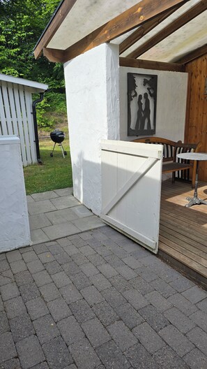 Ein überdachter Patio-Bereich mit einer weißen Wand, einer Holzbank und einem Grill.