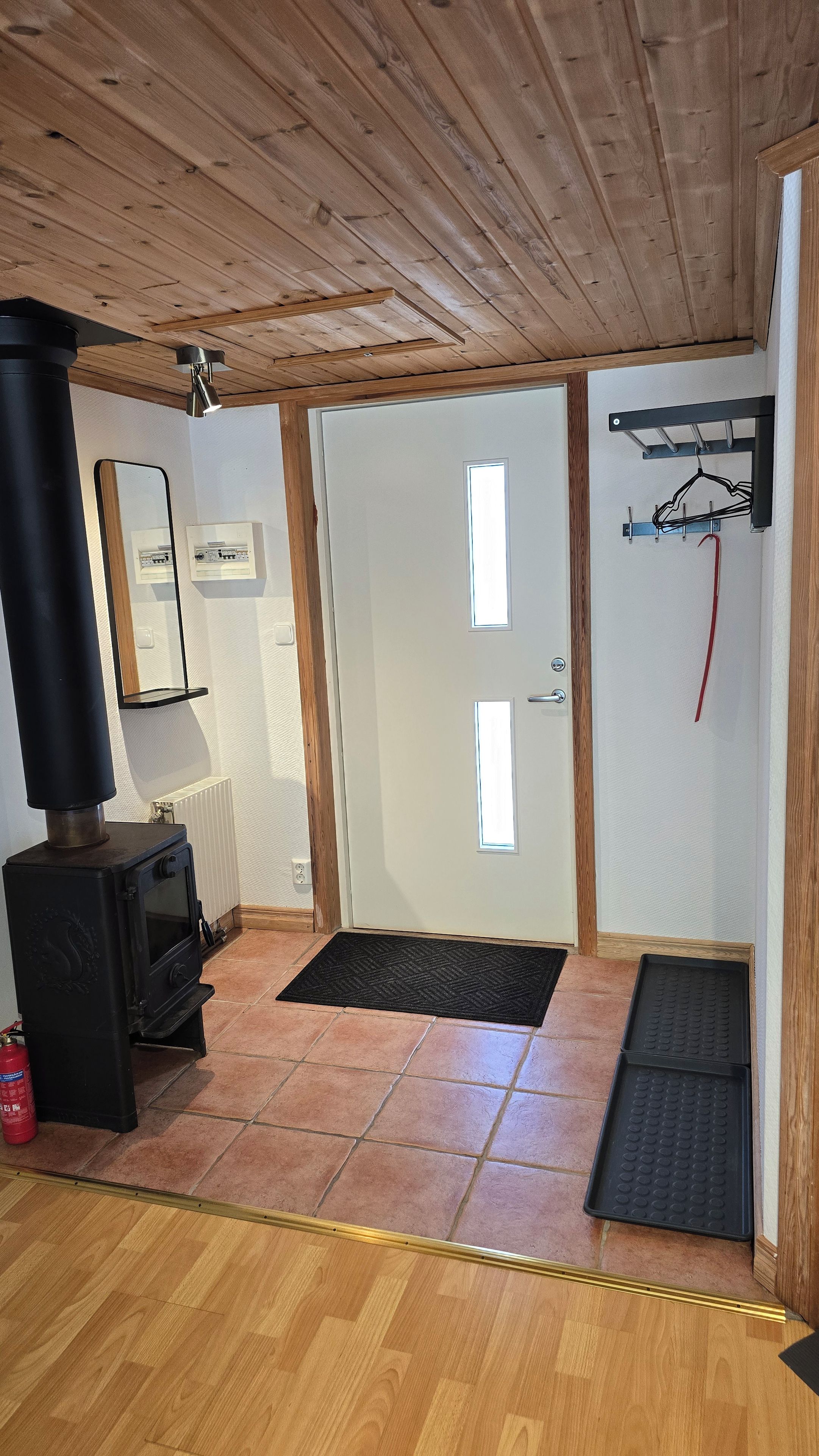 Ein Zimmer mit Kaminofen, einer Tür mit Fenster, einem Heizkörper und einem Kleiderständer.