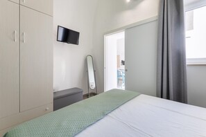 Un dormitorio con cama, armario, espejo y televisor en la pared.