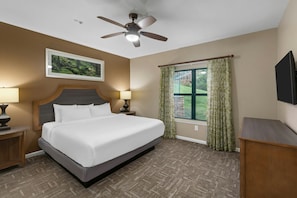 A hotel room with a bed, two bedside tables, a ceiling fan, a window with curtains, and a mounted flat-screen TV. - 2BR/2BA Smoky Mountains Resort Suite · Indoor Pool & Hot Tubs · Sleeps 8 (Sevierville)
