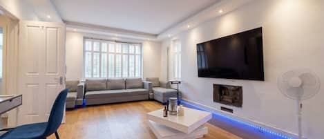 A modern living room with a flat-screen TV, a sofa, a coffee table, and a fan.