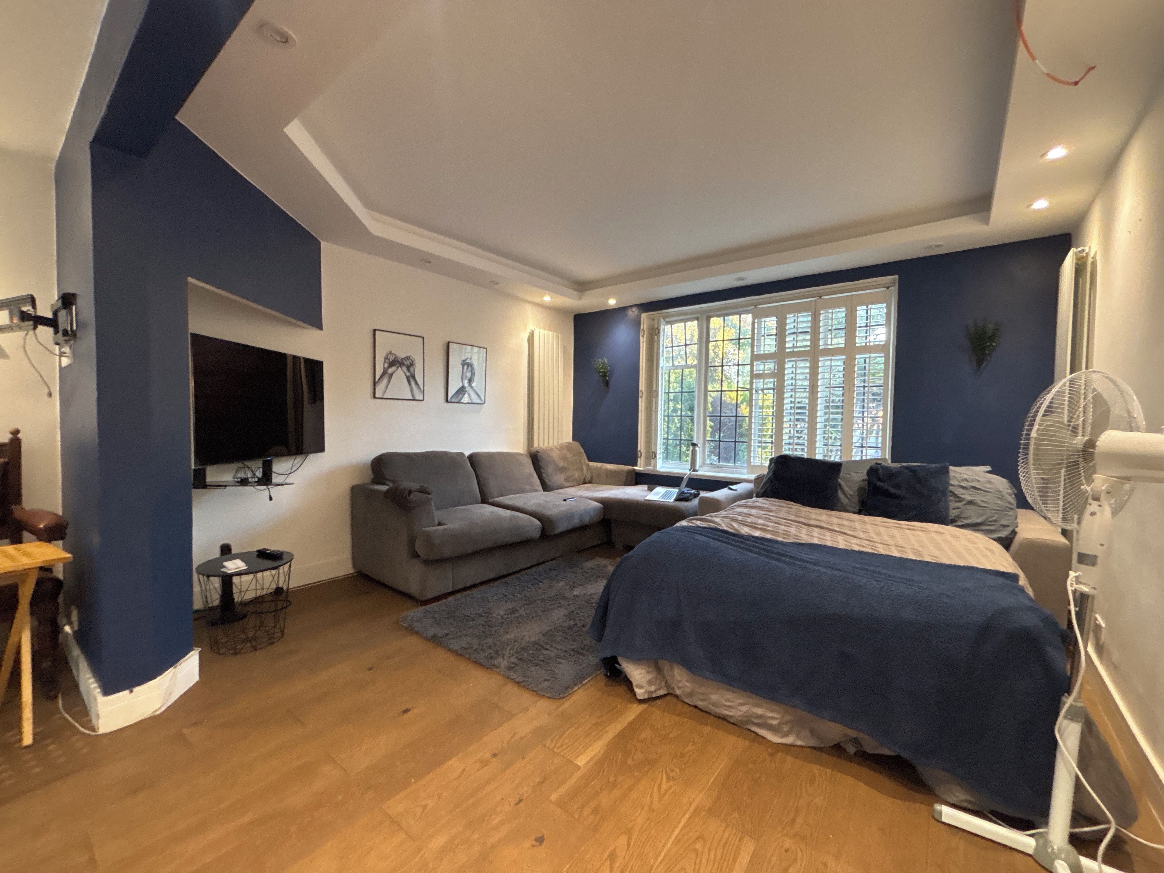 Une chambre moderne avec un lit, un canapé, une télévision et une fenêtre équipée de stores.