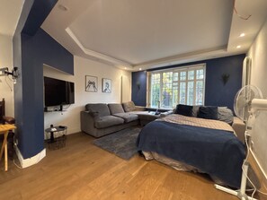 Ein modernes Schlafzimmer mit einem Bett, einer Couch, einem Fernseher und einem Fenster mit Jalousien.