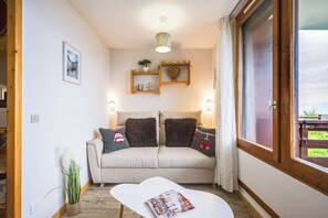 A cozy living room with a sofa, a coffee table, and a window with curtains. - Le Montagnard - Vue Mont Blanc - Pistes (Landry)