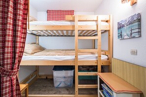 Habitación con literas, una escalera de madera, una mesita pequeña y un baúl para guardar objetos.