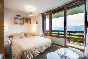 Een hotelkamer met een bed, een klein tafeltje, een raam met uitzicht op bergen en een balkon.