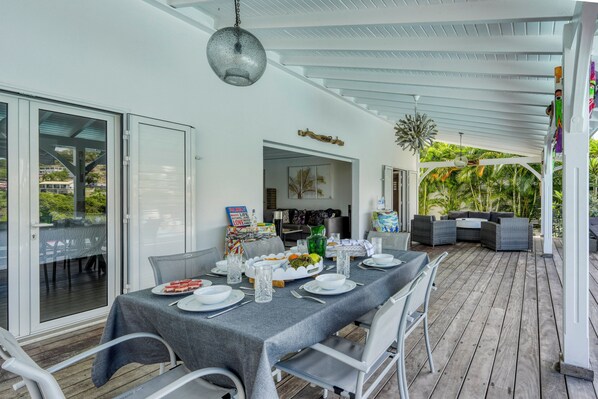 An outdoor dining area with a covered patio, a table set for a meal, and a view of the surrounding greenery. - Villa Corail - Piscine et vue mer - Clim (Le Robert)