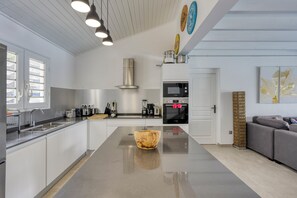 A modern kitchen with a central island, stainless steel appliances, and a built-in oven. - Villa Corail - Piscine et vue mer - Clim (Le Robert)