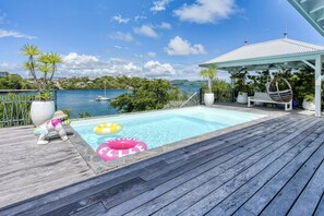 A wooden deck with a swimming pool, lounge chairs, and a view of the sea. - Villa Corail - Piscine et vue mer - Clim (Le Robert)