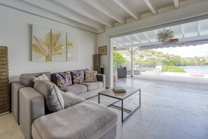 Ein modernes Wohnzimmer mit einem grauen Sofa, bunten Kissen und einem Couchtisch. Ein großes Fenster bietet Blick auf einen See und Gebäude.