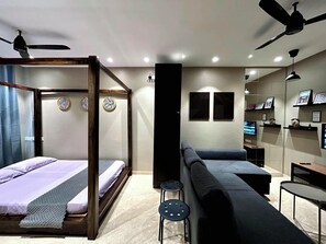 Un dormitorio moderno con cama con dosel, un sofá, un televisor y un ventilador de techo.