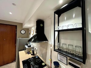 Una cocina con estufa a gas, campana extractora negra y estante con vasos.