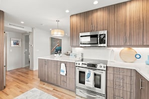 Una cocina moderna con gabinetes de madera, electrodomésticos de acero inoxidable y encimera blanca.