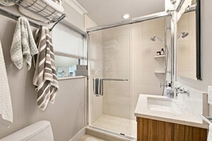 A modern bathroom with a glass-enclosed shower, a white sink, and a towel rack with patterned towels. - Downtown Naples Walkable Escape – Private Lanai, Steps to Beach & 5th Avenue (Naples)