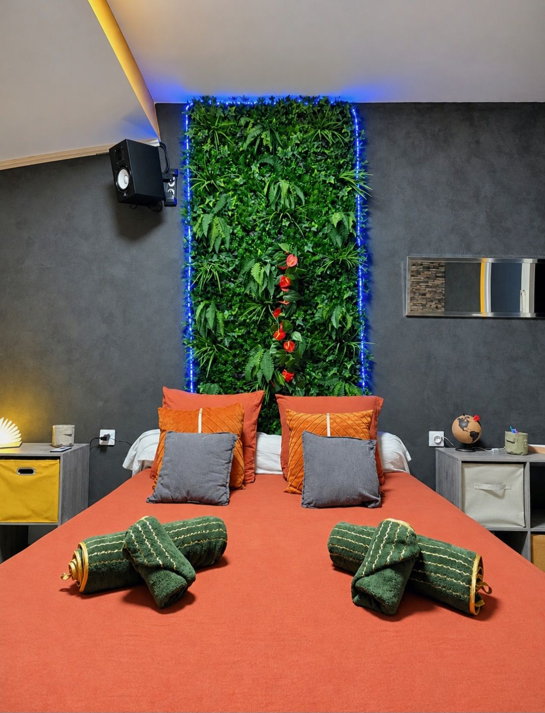 Een moderne slaapkamer met een groene muur, een bed met oranje beddengoed en een klein nachtkastje met een wereldbol.