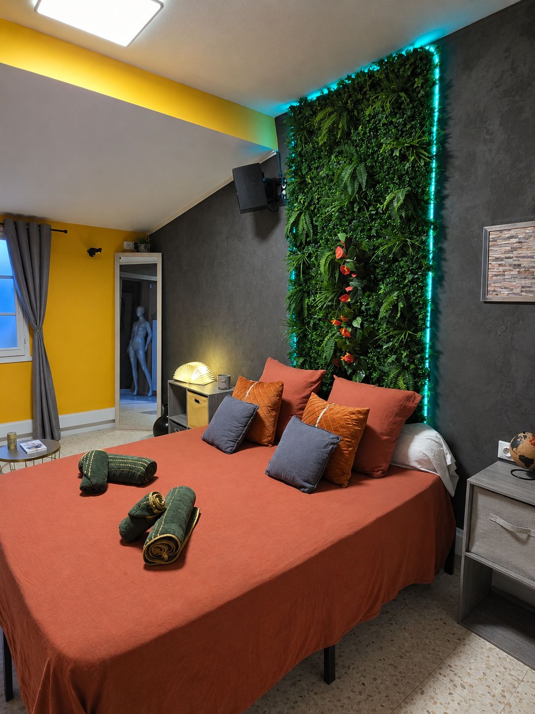 Een slaapkamer met een bed, kussens, een wandtelevisie, een wereldbol en een plantenwand met LED-verlichting.