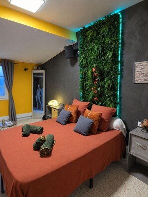 Un dormitorio con cama, almohadas, un televisor montado en la pared, un globo terráqueo y una pared verde con luces LED.