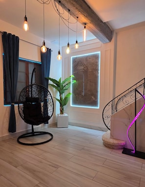 Een modern interieur met een houten vloer, een zwarte stoel, een potplant, een groot raam en een wenteltrap met neonverlichting.