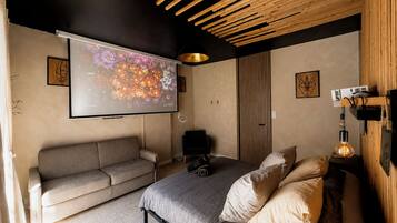 Un dormitorio moderno con cama, sofá, pantalla de proyector y techo de madera.
