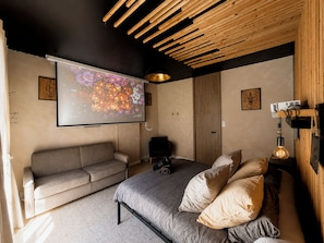 Een moderne slaapkamer met een bed, een bank, een projectiescherm en een houten plafond.