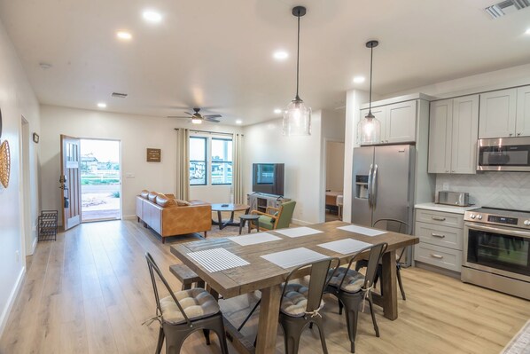Una cocina moderna con electrodomésticos de acero inoxidable, un comedor con mesa y sillas de madera, y una sala de estar con sofá y televisor.