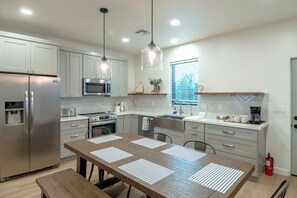 Una cocina moderna con electrodomésticos de acero inoxidable, una mesa de comedor de madera e iluminación colgante.