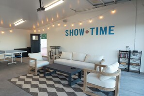Una sala moderna con sofá, mesa de centro, sillas, una mesa de ping pong, una estantería y una pared con el texto 'SHOW TIME'.