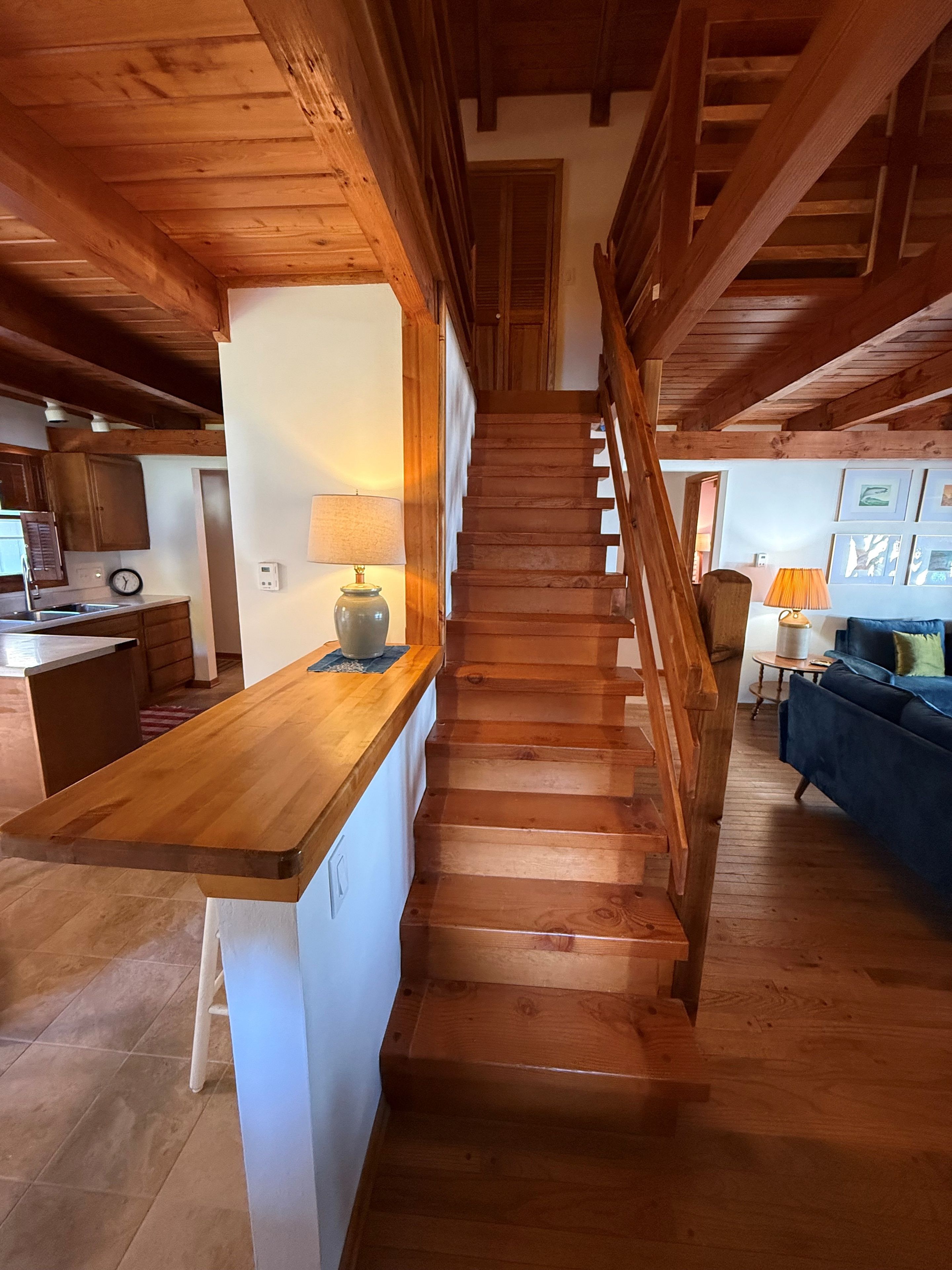 A wooden staircase leading to a second floor, with a kitchen area on the left and a living room on the right.
