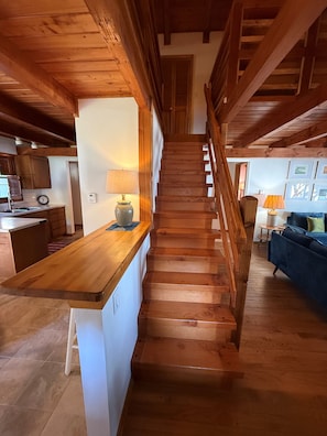 A wooden staircase leading to a second floor, with a kitchen area on the left and a living room on the right. - Jacksonport Sandy Beach Cottage (Baileys Harbor)