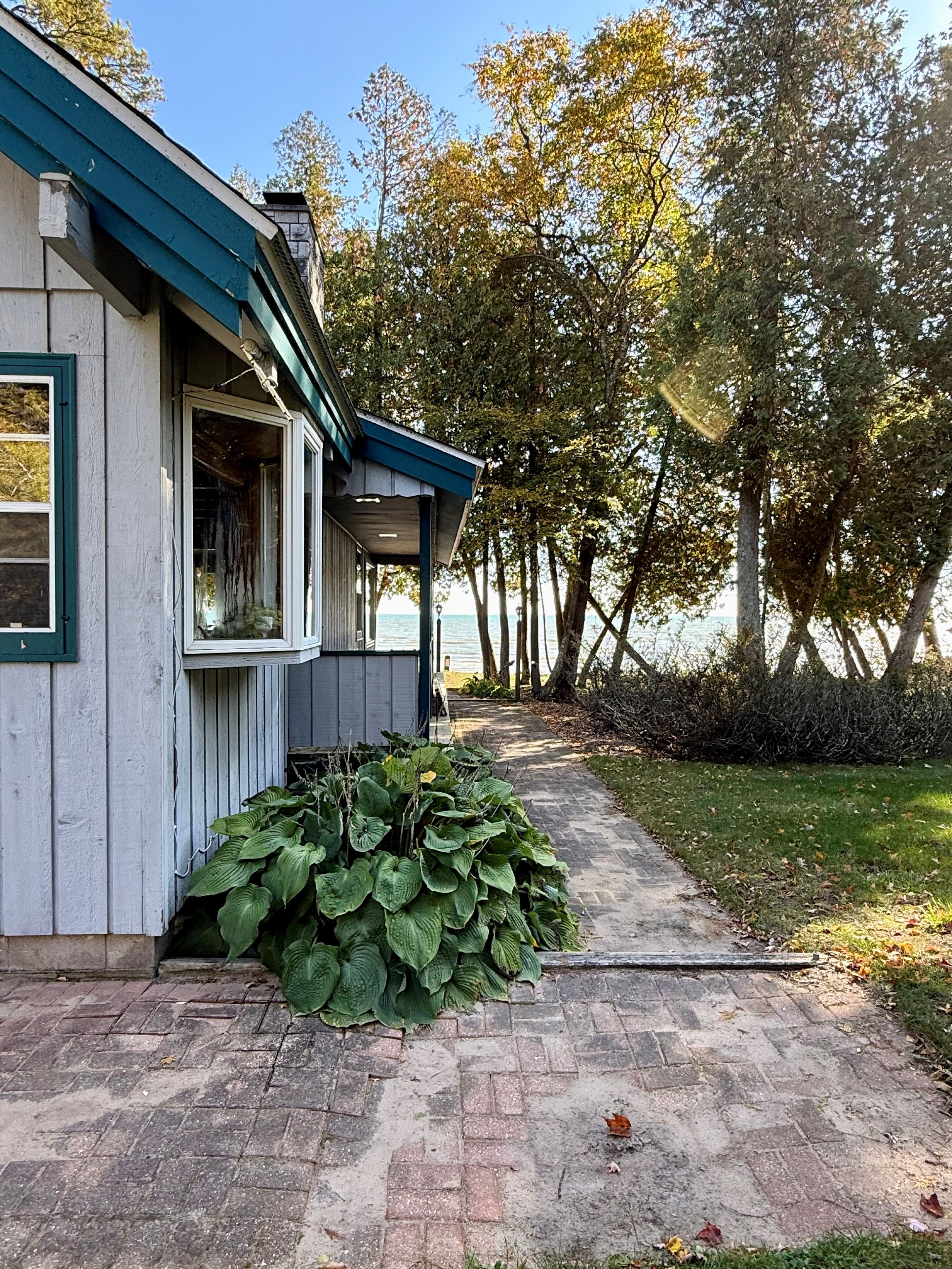 A house with a covered porch and a brick pathway leading to a body of water.