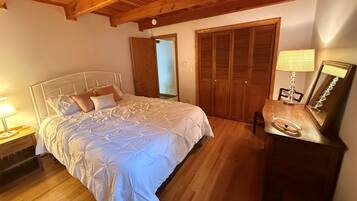 A bedroom with a wooden ceiling, a bed with white bedding, a bedside table with a lamp, and a wooden wardrobe.