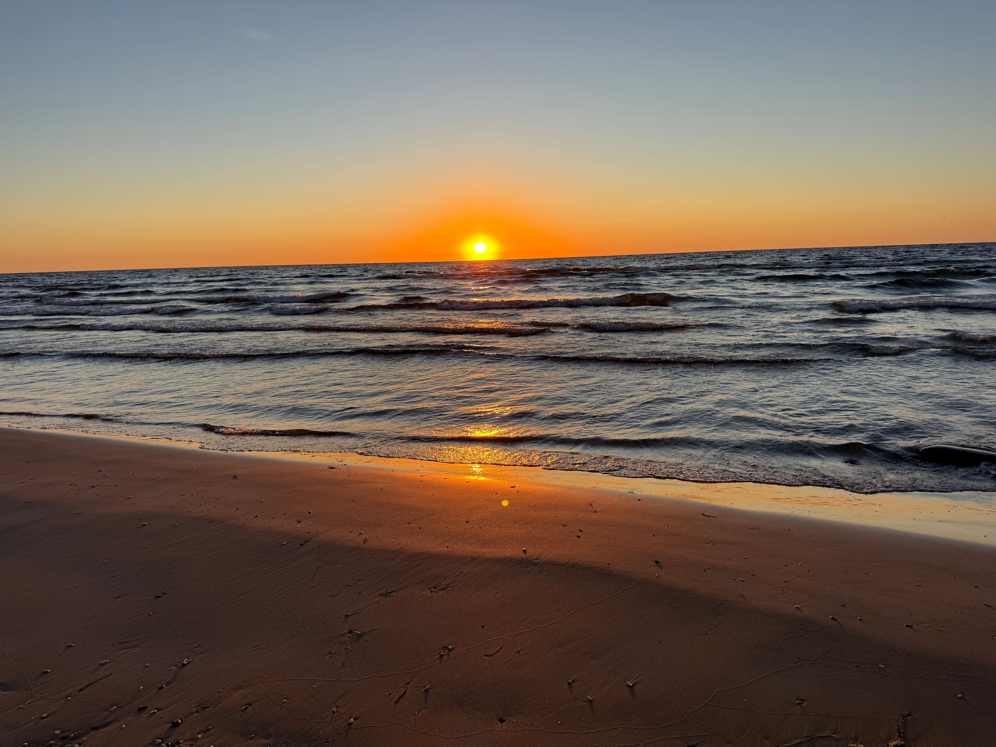 A beach with the sun setting over the ocean, waves gently lapping at the shore.
